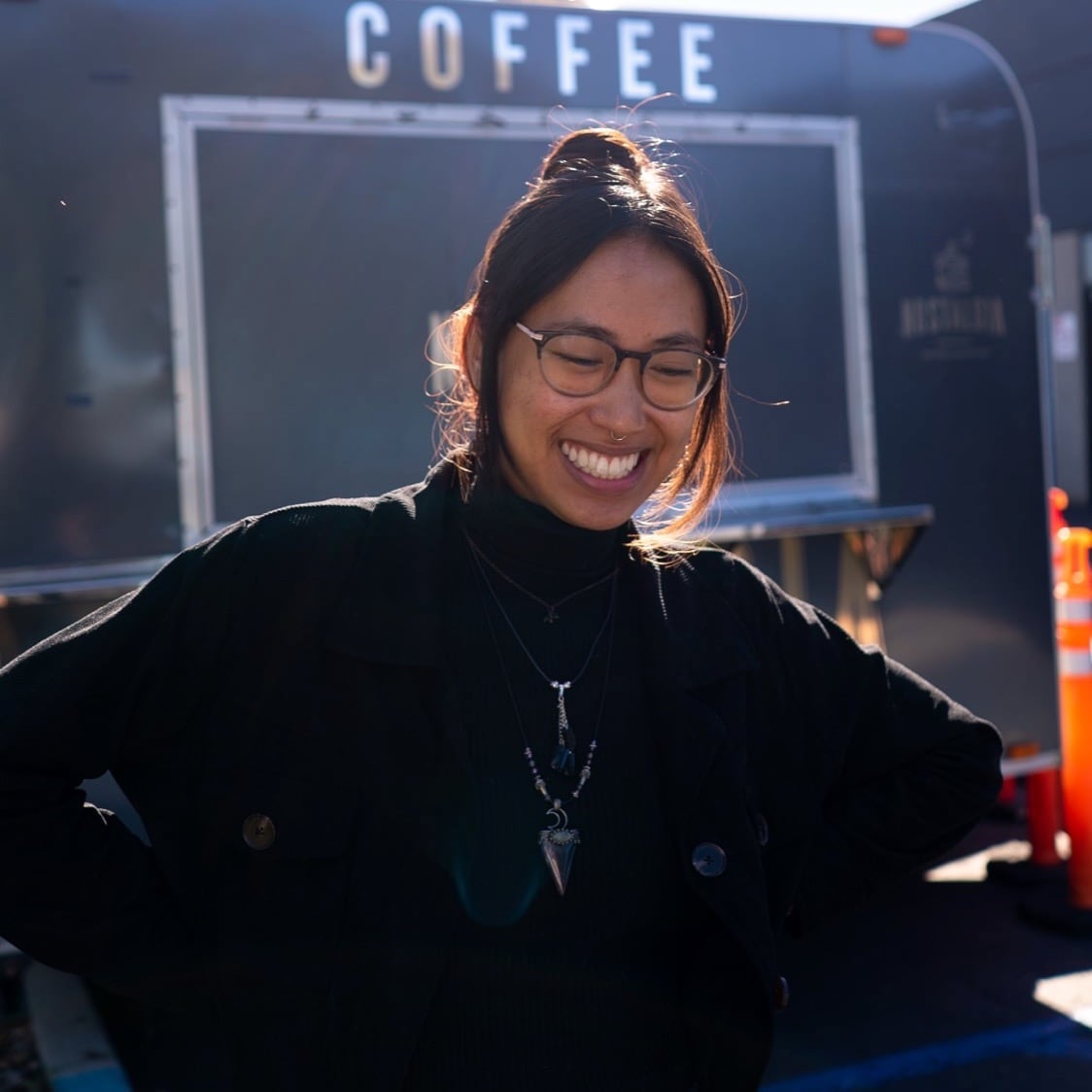 Juslene, wearing glasses, smiling in the sun in front of the Nostalgia Coffee Truck
